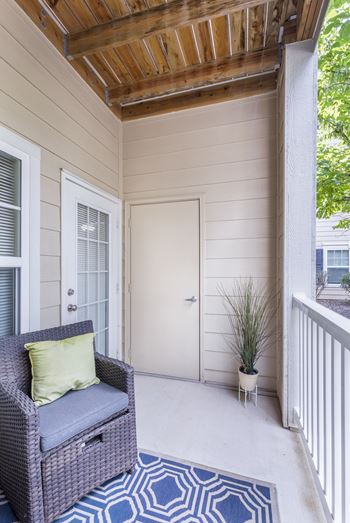 A balcony with a wicker chair and a pillow.